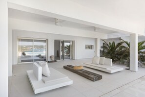 Un salon moderne avec des canapés blancs, un banc en bois et une vue sur la mer, visible à travers de grandes portes vitrées.
