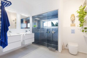 A modern bathroom with a glass shower enclosure, white fixtures, and a blue towel. - Villa Hastinapura: exclusivas vistas al mar, tranquilidad, lujo y arte en Es Castell (Es Castell)
