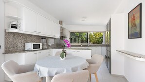 Une cuisine moderne avec des meubles blancs, un plan de travail en granit et un coin repas comprenant une table ronde et des chaises.