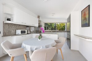 Une cuisine moderne avec des meubles blancs, un plan de travail en granit et un coin repas comprenant une table ronde et des chaises.