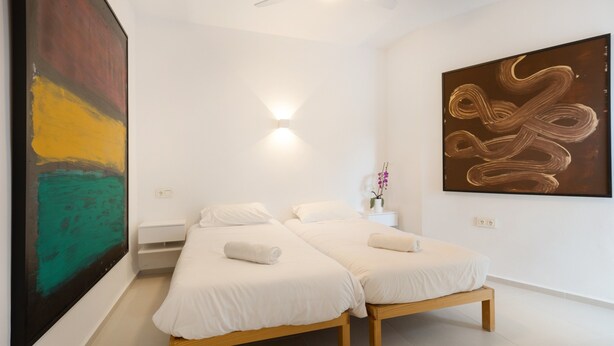 Une chambre d’hôtel moderne avec deux lits, une grande peinture abstraite et un ventilateur de plafond.