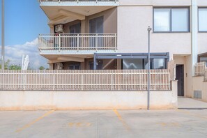 A multi-story building with a balcony, a gated entrance, and a parking area.