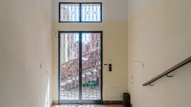 A staircase leading to a door with a metal gate, a trash bin, and a handrail.