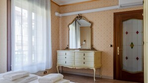 A hotel room with a bed, a dresser, a mirror, and a door with a decorative glass panel.