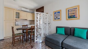 A compact living space with a kitchenette, dining area, and a grey sofa with teal cushions.