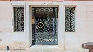 A building entrance with a metal gate, two windows with circular patterns, and a number '961' above the door.