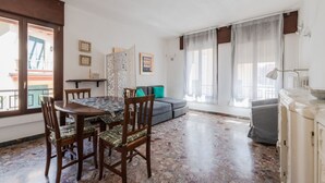 A room with a dining table, chairs, a sofa, a cabinet, and a window with curtains.