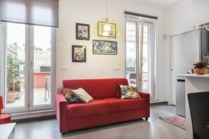 Un canapé rouge agrémenté de plusieurs coussins, un luminaire suspendu et des œuvres d’art encadrées accrochées au mur.