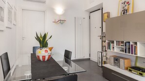 A modern room with a glass table, chairs, a bookshelf, and a potted plant.