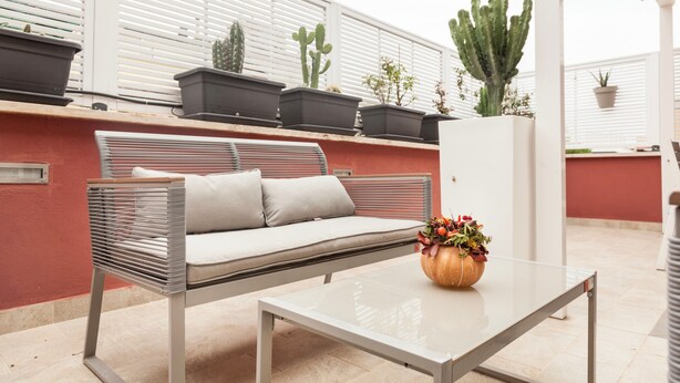 A modern outdoor seating area with a sofa, a table, and potted plants.