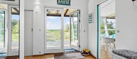 Een modern interieur met een houten vloer, een eethoek met een tafel en stoelen, en een grote glazen deur die uitkomt op een terras met uitzicht op het landschap.