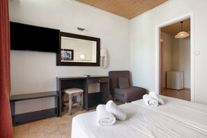 A hotel room with a bed, a desk, a chair, a mirror, a telephone, and a door leading to another room.