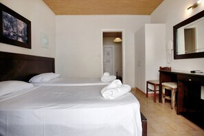A hotel room with two beds, a desk, a chair, a mirror, and a door leading to another room.
