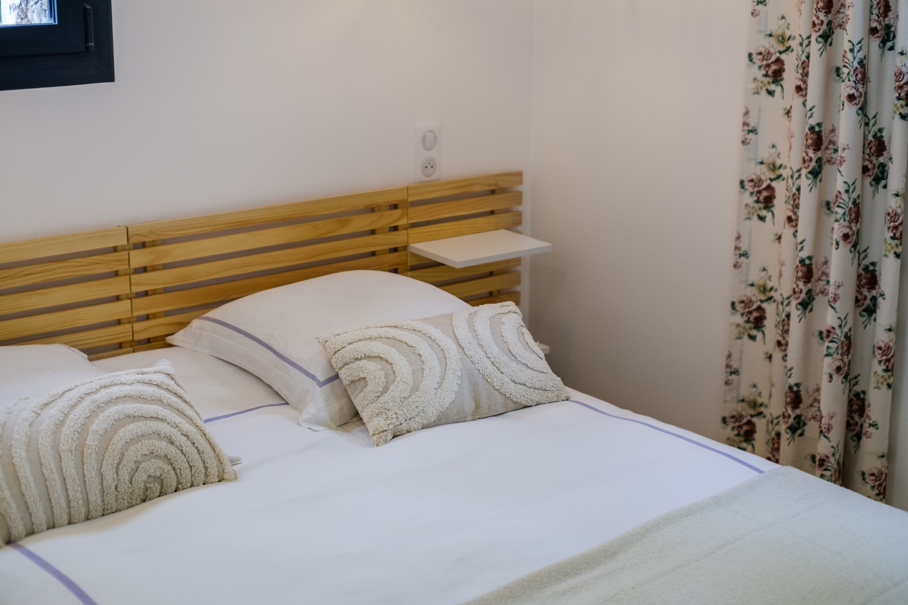 Una cama con cabecera de madera, una mesita de noche pequeña y cortinas con estampado floral.