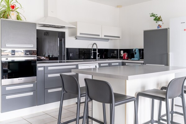 A modern kitchen with grey cabinetry, a large island with bar stools, and a built-in oven.