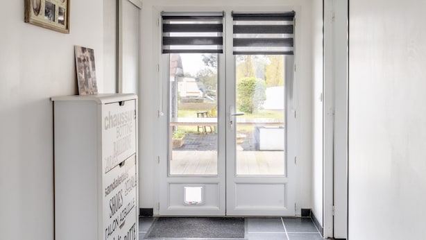 Un pasillo con una puerta doble, un armario blanco con etiquetas y una ventana pequeña.