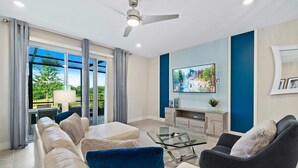 Uma sala de estar moderna com sofá, poltrona, mesa de centro de vidro e televisão de tela plana na parede.