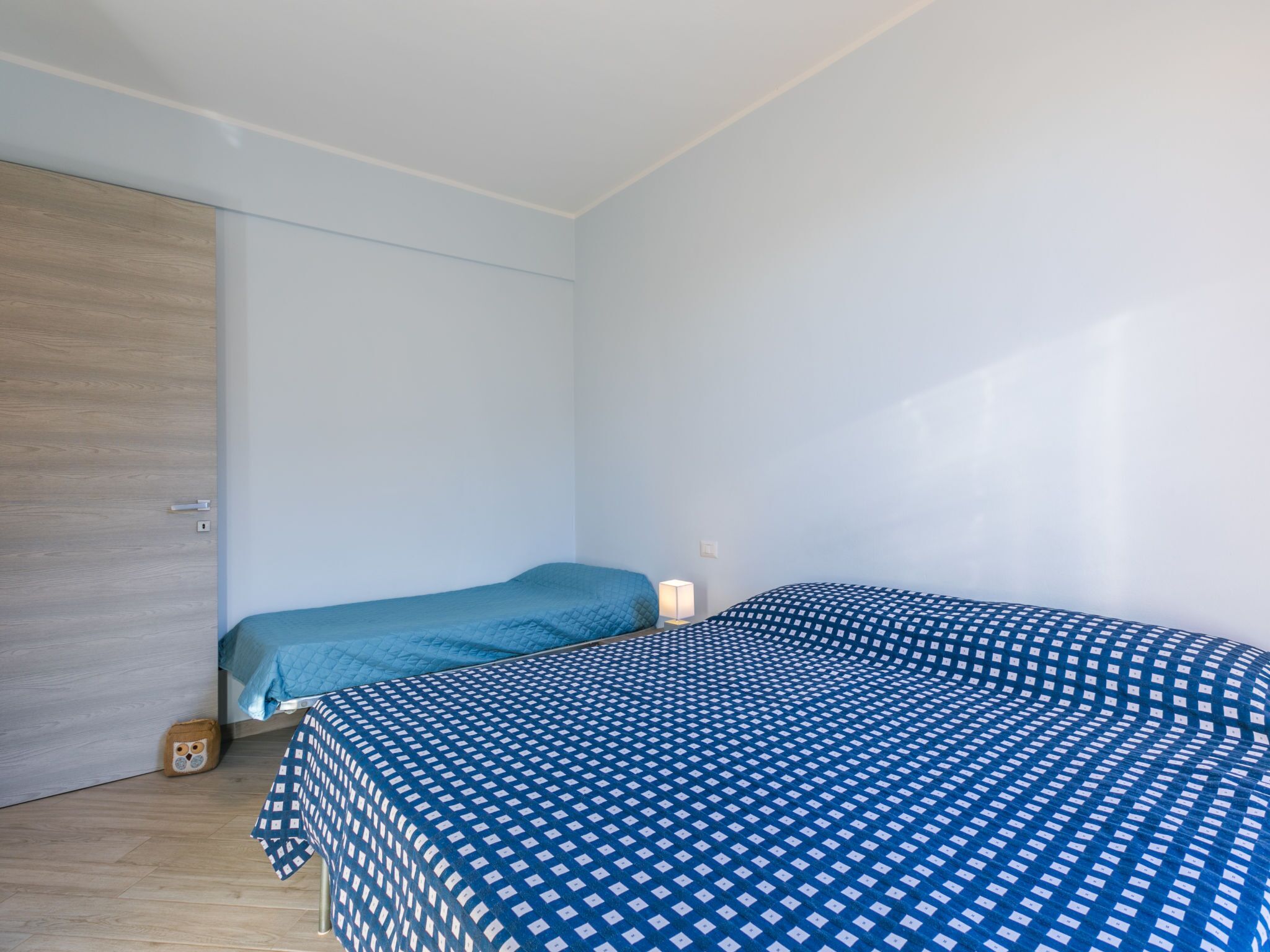 Una piccola camera con un letto singolo, una porta in legno e una parete di colore chiaro.