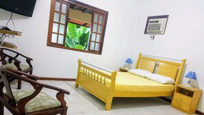 Una habitación con una cama y una silla de madera, una mesita pequeña y un televisor en la pared.