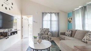 A modern living room with a flat-screen TV, a round coffee table, a patterned armchair, and a beige sofa. - Tranquil Montego Bay City Getaway with Patio: The Perfect Stay! (Montego Bay)