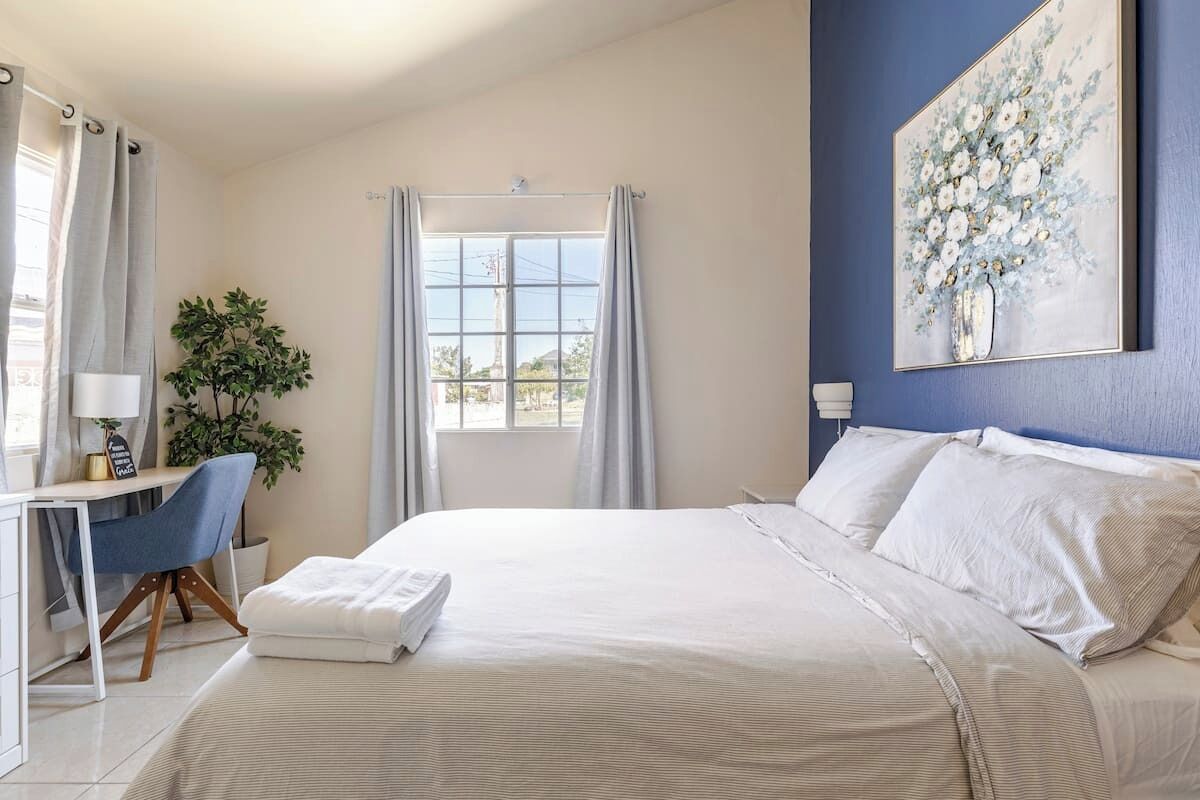 Une chambre à coucher avec un grand lit, un bureau avec une chaise, une plante en pot et une fenêtre avec des rideaux.