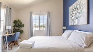 A bedroom with a large bed, a desk with a chair, a potted plant, and a window with curtains. - Tranquil Montego Bay City Getaway with Patio: The Perfect Stay! (Montego Bay)