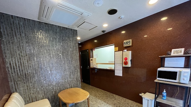 A hotel room with a sofa, a wooden chair, a microwave, a water dispenser, and a small table with a sign. - HOTEL FLOR (Utsunomiya)