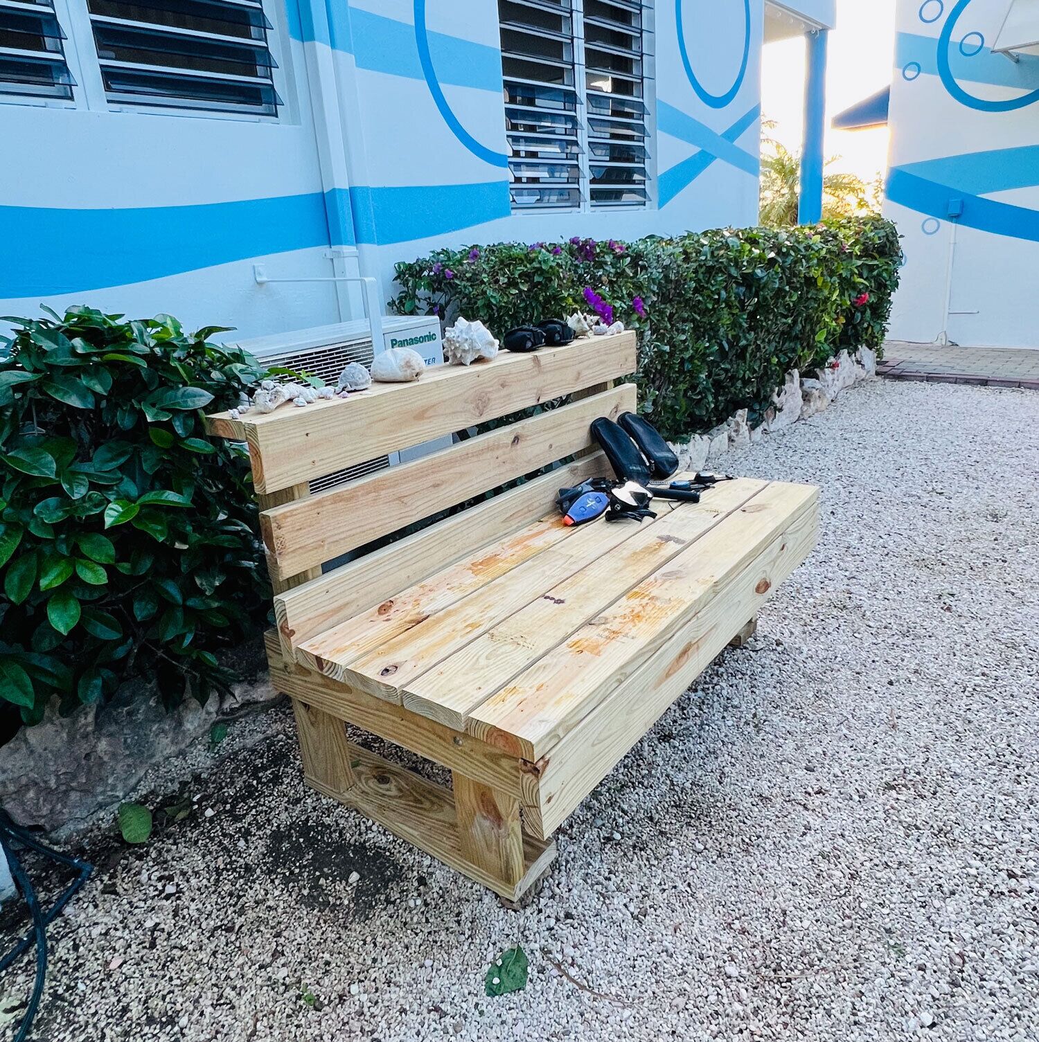 A wooden bench with a Panasonic sign, surrounded by gravel and greenery.