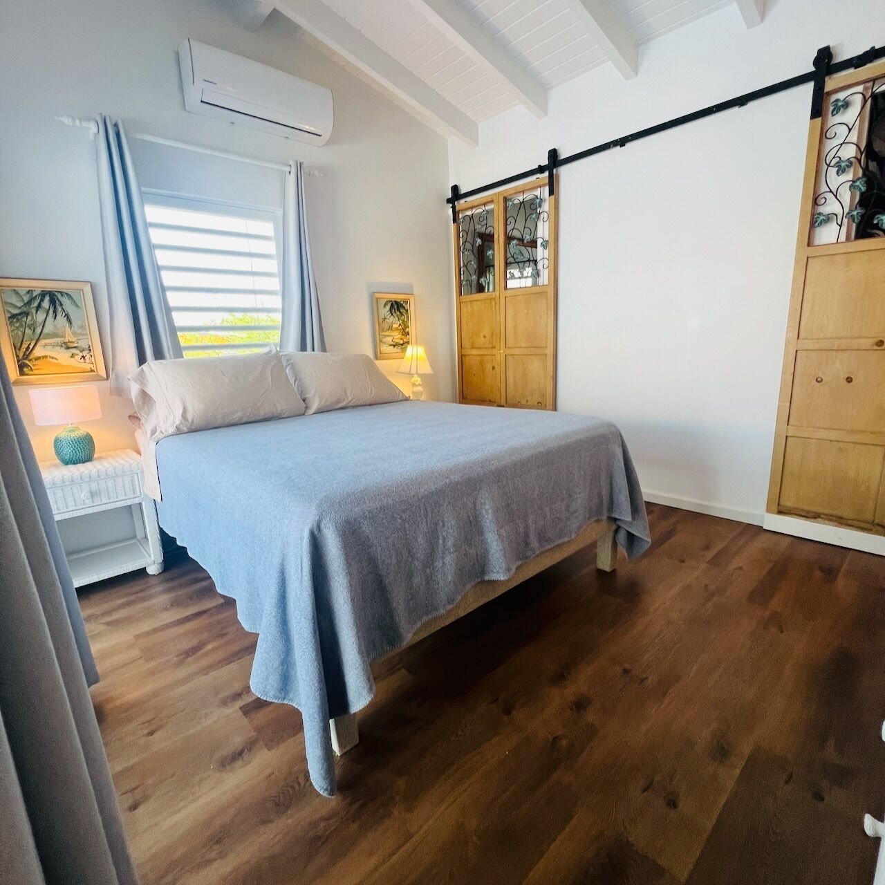 A bedroom with a bed, a nightstand, a lamp, a wardrobe, and a window with curtains.