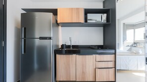 A modern kitchen with a stainless steel refrigerator, wooden cabinets, a black countertop, and a microwave. - Vn Oscar Freire (São Paulo)