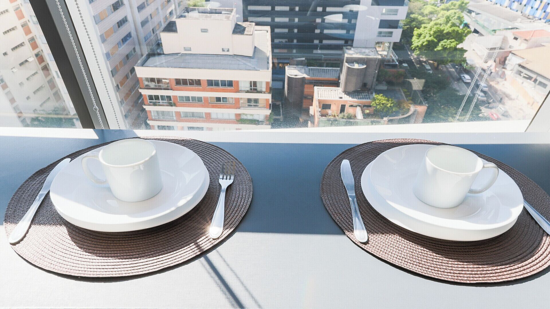 Una mesa con dos tazas y platillos blancos, con vistas a edificios y un árbol.