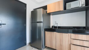 A modern kitchen with a stainless steel refrigerator, wooden cabinets, a black countertop, and a microwave.