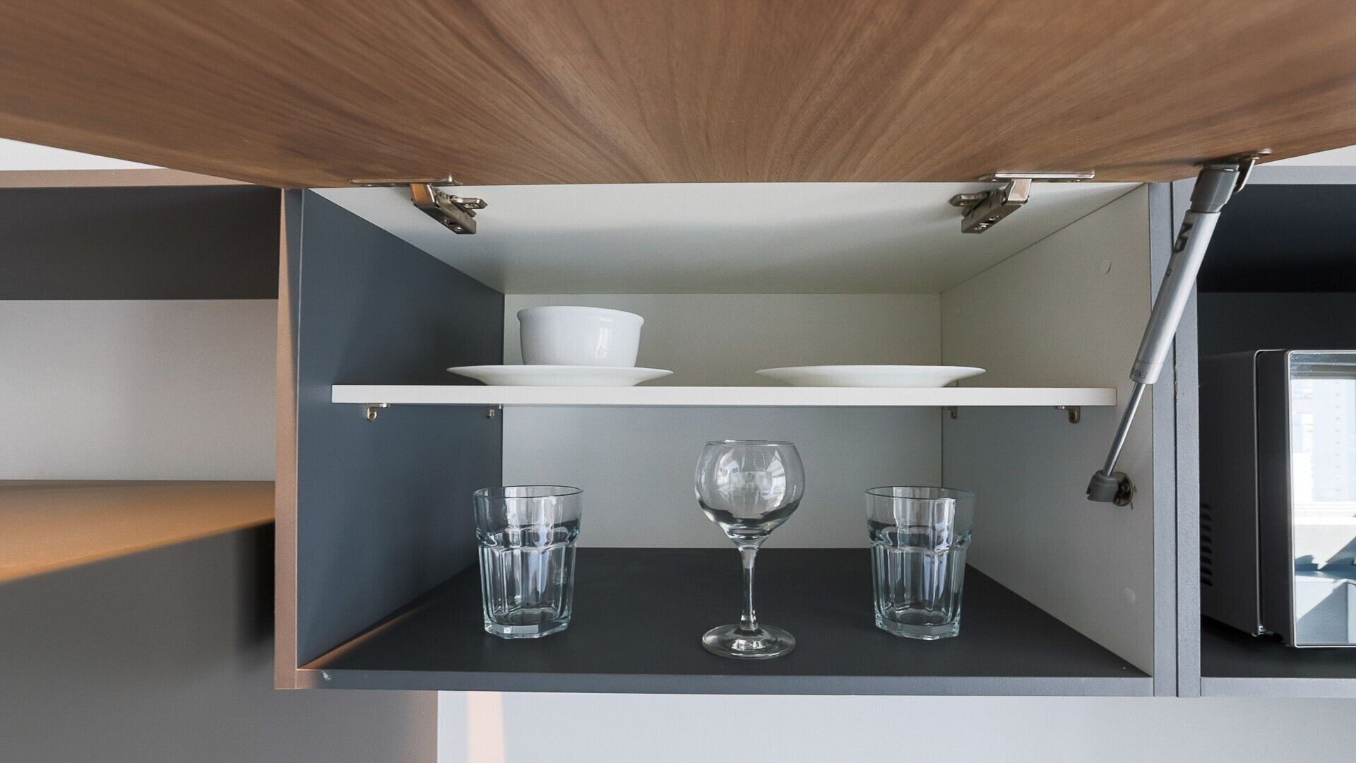 Eine Küche mit einer Holzausziehtafel, einem weißen Regal mit einer Schüssel und einem Weinglas sowie einem Schrank mit einer Glaseinlage.