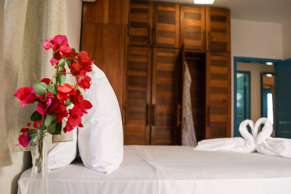 A hotel room with a bed, a vase with red flowers, and wooden wardrobes in the background.