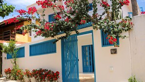 A white building with blue shutters and a blue door, surrounded by red flowers and greenery. - Vila Marinella (Jijoca de Jericoacoara)