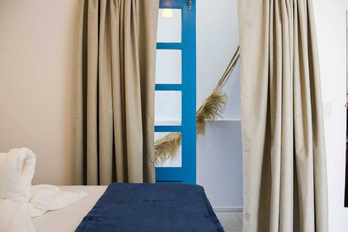 A room with a bed, beige curtains, a blue door, and a decorative plant.