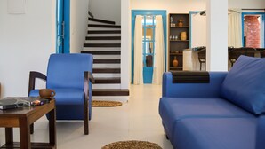 A living room with a blue sofa, a blue armchair, a wooden coffee table, and a staircase with blue doors. - Vila Marinella (Jijoca de Jericoacoara)