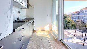 Eine moderne Küche mit Marmor-Spritzschutz, einem schwarzen Wasserhahn und einer Glastür, die auf einen Balkon mit Sitzgelegenheit führt.