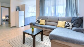 Ein modernes Wohnzimmer mit einer Couch, einem kleinen Tisch und einer Küchenzeile im Hintergrund.