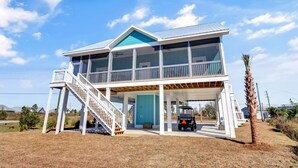 Une maison de plage à deux étages, dotée d’un balcon, d’une véranda et d’un véhicule tout-terrain.