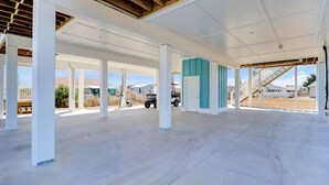 Un espace extérieur abrité, doté d’un sol en béton et de piliers blancs, comprenant un escalier et offrant une vue sur un quartier résidentiel.