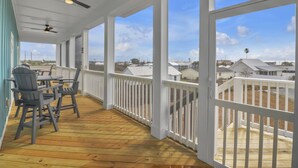 Une véranda couverte avec un plancher en bois, des balustrades blanches et des ventilateurs de plafond.
