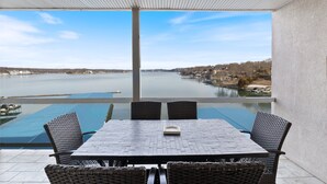 Une terrasse avec une table et des chaises donnant sur un lac, offrant une vue dégagée sur l’eau et les bâtiments situés au loin.