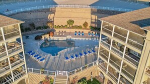 Un espace piscine doté de chaises longues bleues et d’une fontaine centrale, le tout entouré d’un bâtiment à plusieurs étages et agrémenté de balcons.