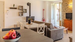 A modern living room with a dining area, a fireplace, a stone wall, and a television.