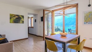 A modern dining area with a wooden table and yellow chairs, a large window with a view of a balcony, and a map on the wall. - La Terrazza sul Lago by Interhome (Bellano)
