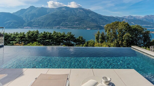 An infinity pool with clear water, a lounge chair, and a book and cup on the edge. - La Terrazza sul Lago by Interhome (Bellano)