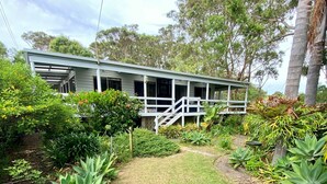 A single-story house with a porch, surrounded by lush greenery and trees.