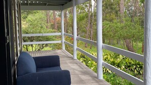 A covered porch with a wooden deck, white railings, and a view of a forested area.