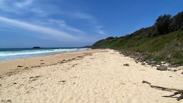 A sandy beach with a rocky shoreline and a grassy hill in the background.